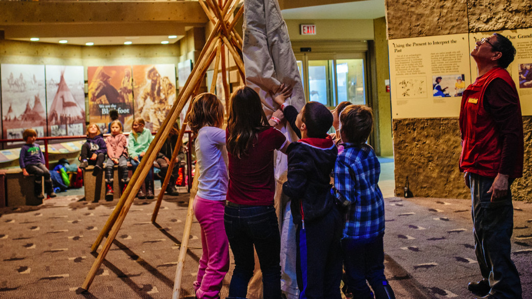 A photo of children constructing a teepee at the Head Smashed-In Buffalo Jump