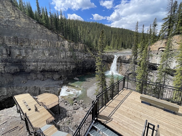 An image of a wooden-floored and railed staircase structure overlooking lush forestry and a waterfall at Crescent Falls Provincial Recreation Area.