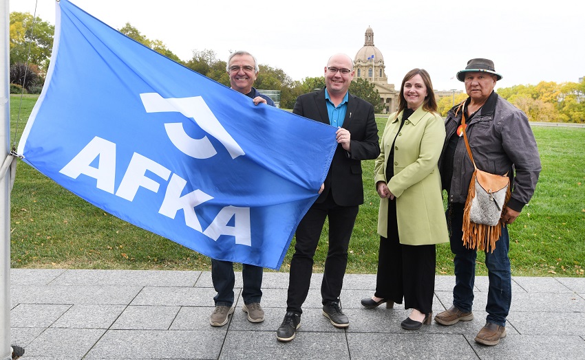 Rene Rajotte, president of the Alberta Foster and Kinship Association (AFKA), Minister of Children and Family Services Searle Turton, AFKA CEO Melissa Jones and Elder Philip Campiou raise a flag commemorating the start of Foster and Kinship Caregiver Month.