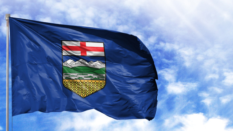 Alberta flag flies at full mast against a blue sky with some clouds.
