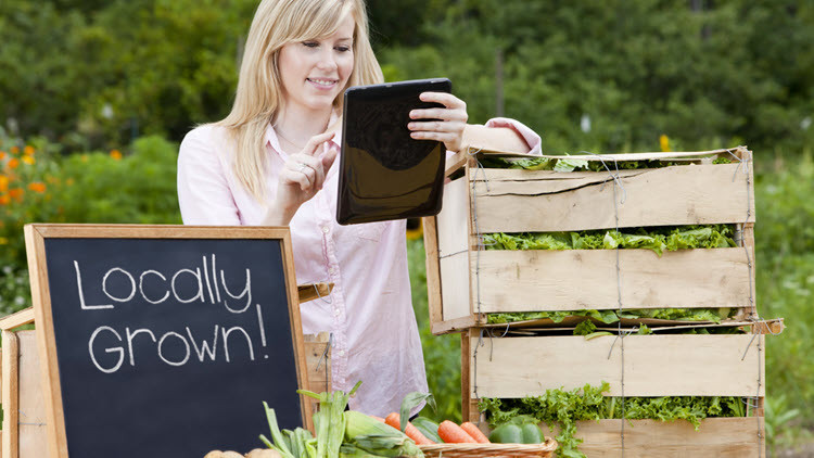 Photo of woman at farmers' market with sign saying locally grown